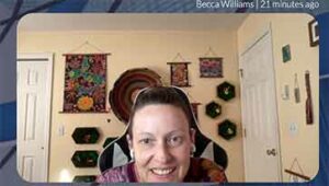 A 40-something white woman with brown hair wearing AirPods accidentally took a selfie from her computer during a metaverse call. She has an amused smile as a result.