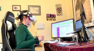 A 40-something white woman with brown hair wearing a green sweater at her desk in her home office wearing a VR headset