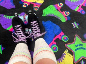 Colorful roller skate patterned carpet at Skate Country in Tucson with two legs in tube socks and black quad skates with purple sparkly laces